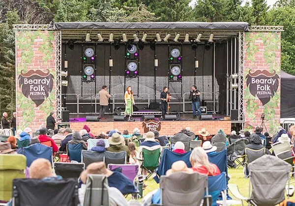 Stage banners on display at Beardy Folk Festival while spectators watch a live band